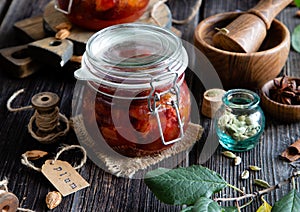 Two glass jars with homemade canned plums jam, marmalade, jelly on rustic wooden table with cardamon, cinnamon,  anise