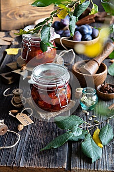 Two glass jars with homemade canned plums jam, marmalade, jelly on rustic wooden table with cardamon, cinnamon,  anise, plums