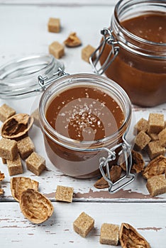 Two glass jars of homemade caramel with crystals of salt and pieces of cane sugar