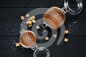 Two glass jars with homemade salted caramel and pieces of brown sugar with salt crystals