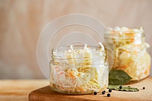 Two glass jars with sauerkraut are standing on wooden cooking board on light background with copy space. photo