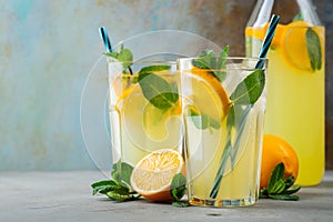 Two glass with lemonade or mojito cocktail with lemon and mint, cold refreshing drink or beverage with ice on rustic blue