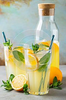 Two glass with lemonade or mojito cocktail with lemon and mint, cold refreshing drink or beverage with ice on rustic blue