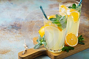 Two glass with lemonade or mojito cocktail with lemon and mint, cold refreshing drink or beverage with ice on rustic blue