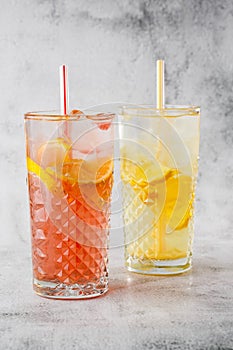 Two glass with lemonade and orange cocktail with lemon and orange, cold refreshing drink or beverage with ice on bright marble