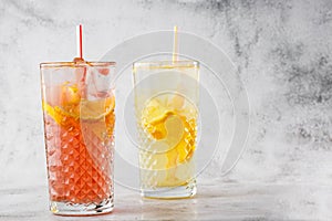 Two glass with lemonade and orange cocktail with lemon and orange, cold refreshing drink or beverage with ice on bright marble