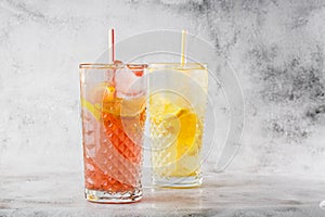 Two glass with lemonade and orange cocktail with lemon and orange, cold refreshing drink or beverage with ice on bright marble