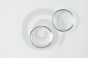 Two glass petri dish with transparent gel with air bubbles and one empty on white background, top view and copy space