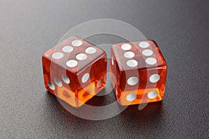 Two glass red dice lie on a black matte table with a light source on top in the left corner.