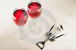 Two glass of red wine and corkscrew on white marble background/Two glass of red wine and wooden corkscrew on white marble