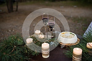 Two glass with red wine, wedding cake and a lot of candles decorated with pine branches. Romantic dinner for couple. .