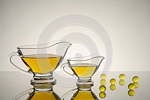 Two glass saucers of different sizes with yellow sauce, on a glossy surface with reflections, next to yellow transparent balls