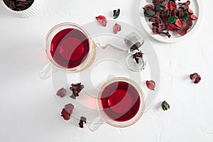 Two glass transparent cups of hibiscus red tea on a white background with dried rose petals. top view. the concept of weight loss