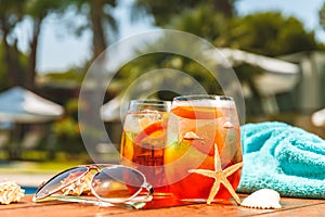 Two glasses of aperol spritz or negroni cocktail with seashells, towel and sunglasses