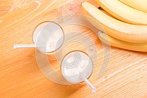 Two glasses of banana juice on the table next to a yellow ripe b