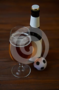 Two glasses with beer, bottles, snacks and soccer ball on wooden table.