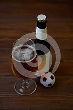 Two glasses with beer, bottles, snacks and soccer ball on wooden table.