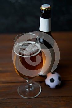 Two glasses with beer, bottles, snacks and soccer ball on wooden table.