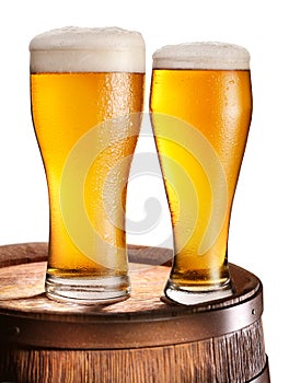 Two glasses of beer over woden barrel.