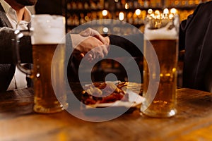 two glasses of beer on the table, greeting friends by the hand, evening in the pub, close-up