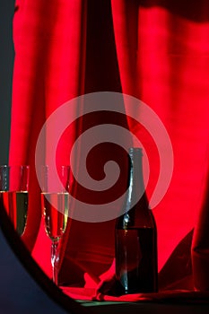 two glasses and a bottle are sitting in front of a red curtain
