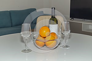 Two glasses, a bottle of white wine and a bowl of oranges close-up