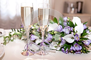 Two glasses of champagne and a bouquet of lilac freesias and white callas.