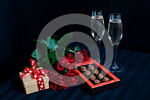 Two glasses with champagne and a bouquet of red roses and candies on the black background