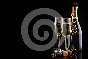 Two glasses of champagne, candles and a bottle on a black background.