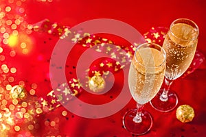 Two glasses of champagne and chocolate in golden wrapper on a red velvet background