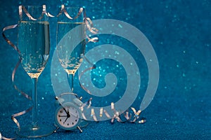 Two glasses of champagne and clock decorated streamers on blue glittering background. Christmas and New Year holidays concept.