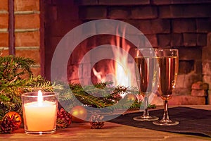 Two glasses of champagne, decorations, Christmas tree branches and a candle on a wooden table in front of a burning