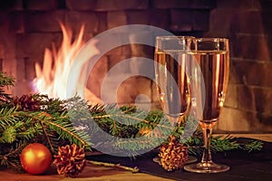 Two glasses of champagne, decorations, Christmas tree branches and a candle on a wooden table in front of a burning