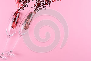 Two glasses of champagne filled with heart shaped sequins on a pink background valentine`s day