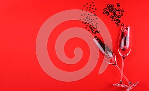 Two glasses of champagne filled with heart shaped sequins on a red background valentine`s day