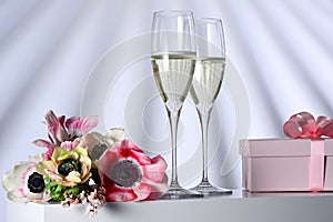 Two glasses with champagne, gift and flowers