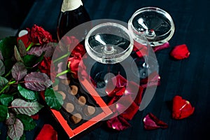 Two glasses of champagne, red roses, petals and chocolates on a black background