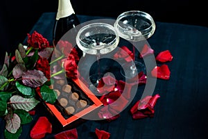 Two glasses of champagne, red roses, petals and chocolates on a black background