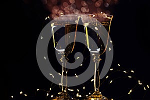 Two glasses with champagne sparkling wine on a dark background and sparkling bokeh. Atmosphere of celebration, magic and happiness