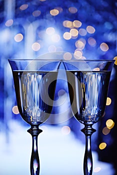 Two glasses with champagne sparkling wine on a festive blue background with lights and bokeh.