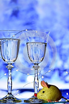 Two glasses with champagne sparkling wine on a festive blue background with lights and bokeh and a toy rat.