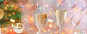 Two glasses of champagne stand on a white wooden table on the background of a New Year tree and garlands. Christmas bokeh.