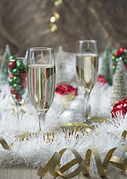 Two glasses of champagne on a table with white tinsel and silver and red Christmas decorations