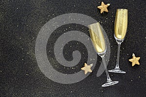 Two glasses of champagne toasting with golden glitter on a black background. Holiday background. Celebrate party concept.