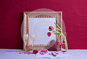 Two glasses with champagne, tulips in a vase, a candlestick with a burning candle, an iron heart, an old photo frame on a red