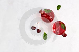 Two glasses of cherry cocktail on a grey background. Fresh cold refreshing summer drink with cherry and ice. Top view