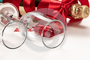 Two glasses close up and a gift bottle of champagne wrapped in a red silk ribbon on a white background