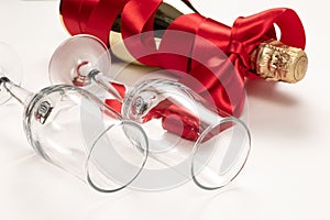 Two glasses close up and a gift bottle of champagne wrapped in a red silk ribbon on a white background