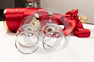 Two glasses close up and a gift bottle of champagne wrapped in a red silk ribbon on a white background