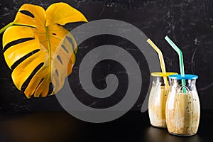 Two glasses with a cocktail. Cocktails with a straw on a black background. Monstera in the background.